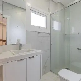 Foto de um banheiro com bancada branca e box de vidro transparente.
