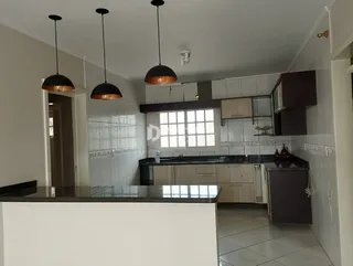 Vista da cozinha e área de jantar com ilha e revestimentos brancos.