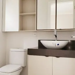 Foto de um banheiro mostrando um vaso sanitário branco e uma bancada escura.