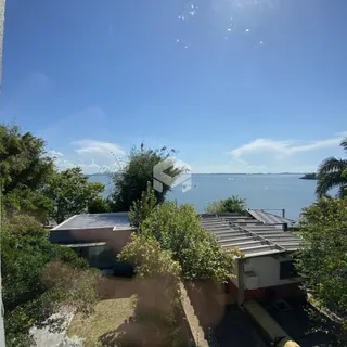 Vista da casa com vegetação e corpo d'água no fundo.