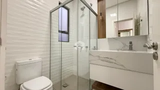 Banheiro moderno com box de vidro e louças brancas.