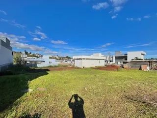 Vista externa de uma propriedade com terreno gramado e construções ao fundo.