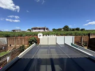 Vista panorâmica de uma área externa com vegetação e uma residência ao fundo.