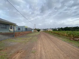 Vista da propriedade rural com estrada de terra e vegetação ao fundo.