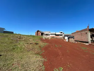 Vista externa de uma propriedade com terreno em terra vermelha e construção em andamento.