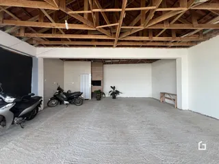 Interior de um espaço amplo com teto de madeira exposto e piso cru.