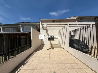 Pátio externo pavimentado com piso de cerâmica e muro branco de uma residência.