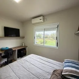 Foto interna de um quarto com cama e televisão montada na parede.