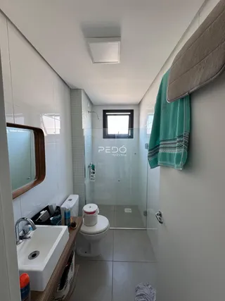 Interior de um banheiro com revestimento cerâmico e box de vidro.