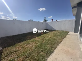 Vista externa mostrando um muro branco e uma área gramada em frente à propriedade.