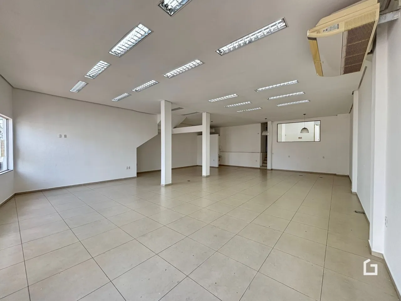 Imagem de um ambiente interno amplo com piso de cerâmica e teto com iluminação em painéis.