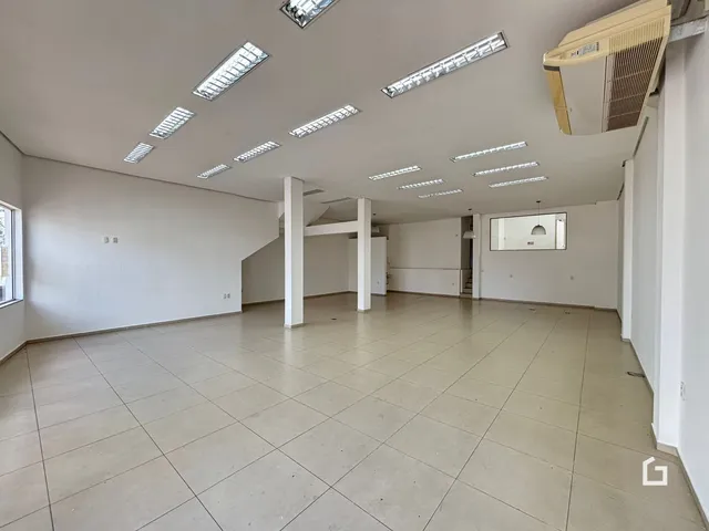 Imagem de um ambiente interno amplo com piso de cerâmica e teto com iluminação em painéis.