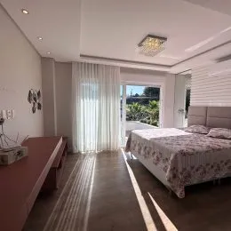 Vista interna de um quarto com cama e cortinas brancas.