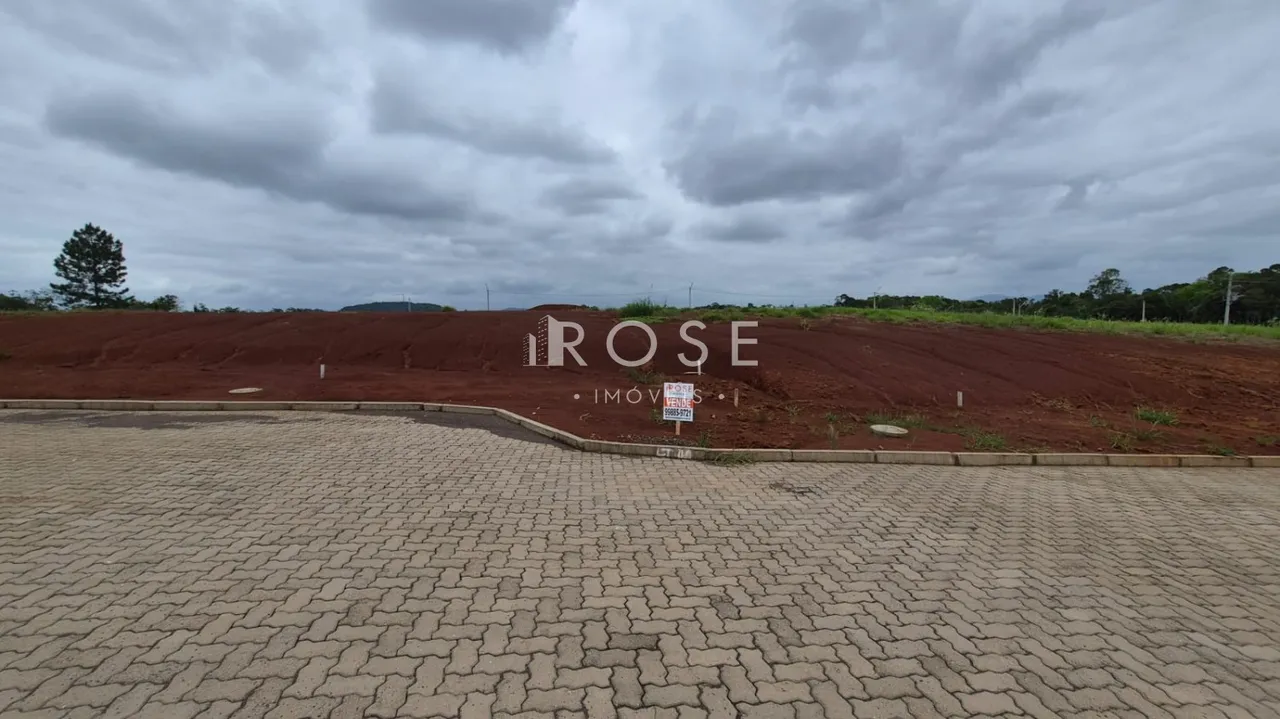 A foto mostra uma área externa de terreno com pavimento e terra avermelhada.