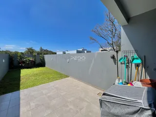 Vista externa de um quintal com gramado e piso de cerâmica.
