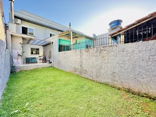 Vista externa de uma residência com um jardim gramado e uma parede de alvenaria.
