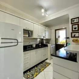 Uma cozinha com armários brancos e bancadas escuras é visível na foto.
