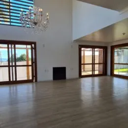 Sala de estar ampla com piso de madeira clara e grandes portas de vidro.
