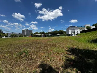 Vista externa de um terreno gramado com estruturas ao fundo sob um céu azul.