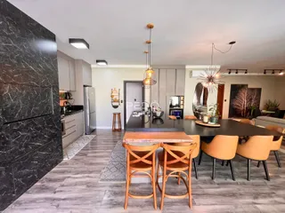 Interior de uma sala de jantar com mesa de madeira escura e cozinha moderna.