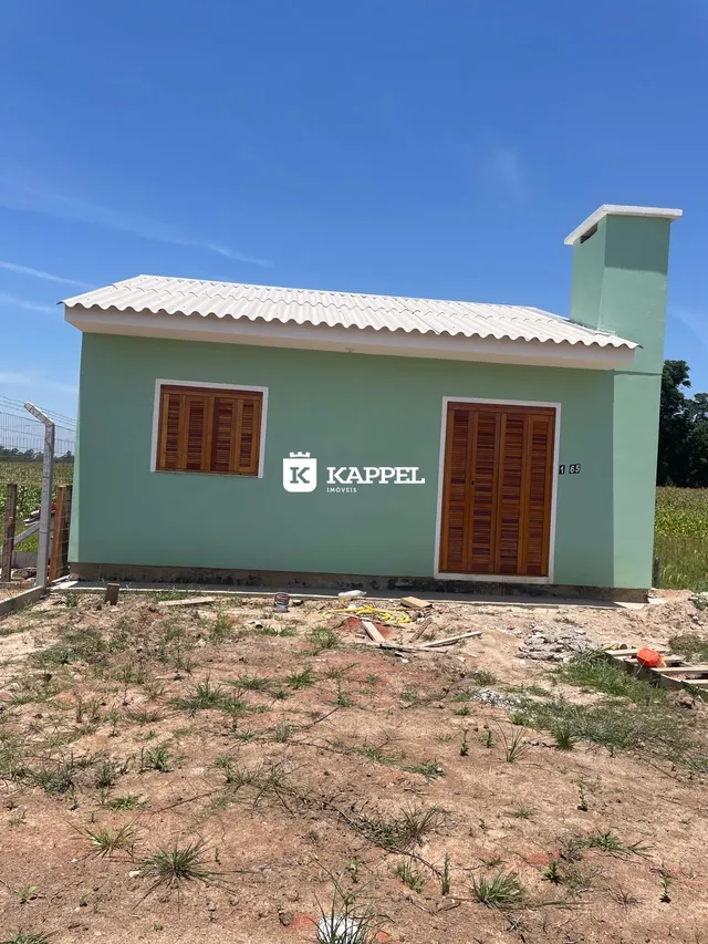 Fachada externa de uma casa em construção com paredes verdes e janelas de madeira.