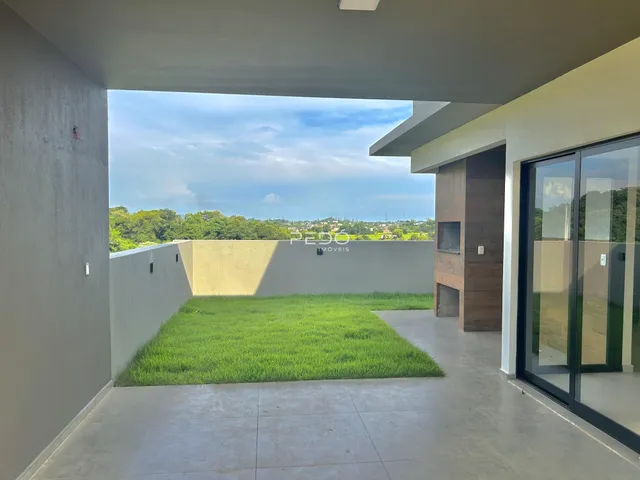 Vista externa de um pátio com gramado verde e muro branco.