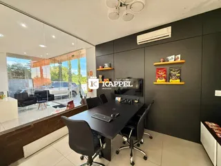 Escritório com mesa grande e vista para o exterior através de grandes janelas.