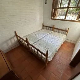 Foto interna de um quarto com cama de madeira e piso de cerâmica.
