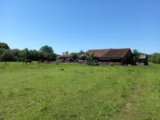 Vista de um campo verde com estruturas rústicas de madeira ao fundo.