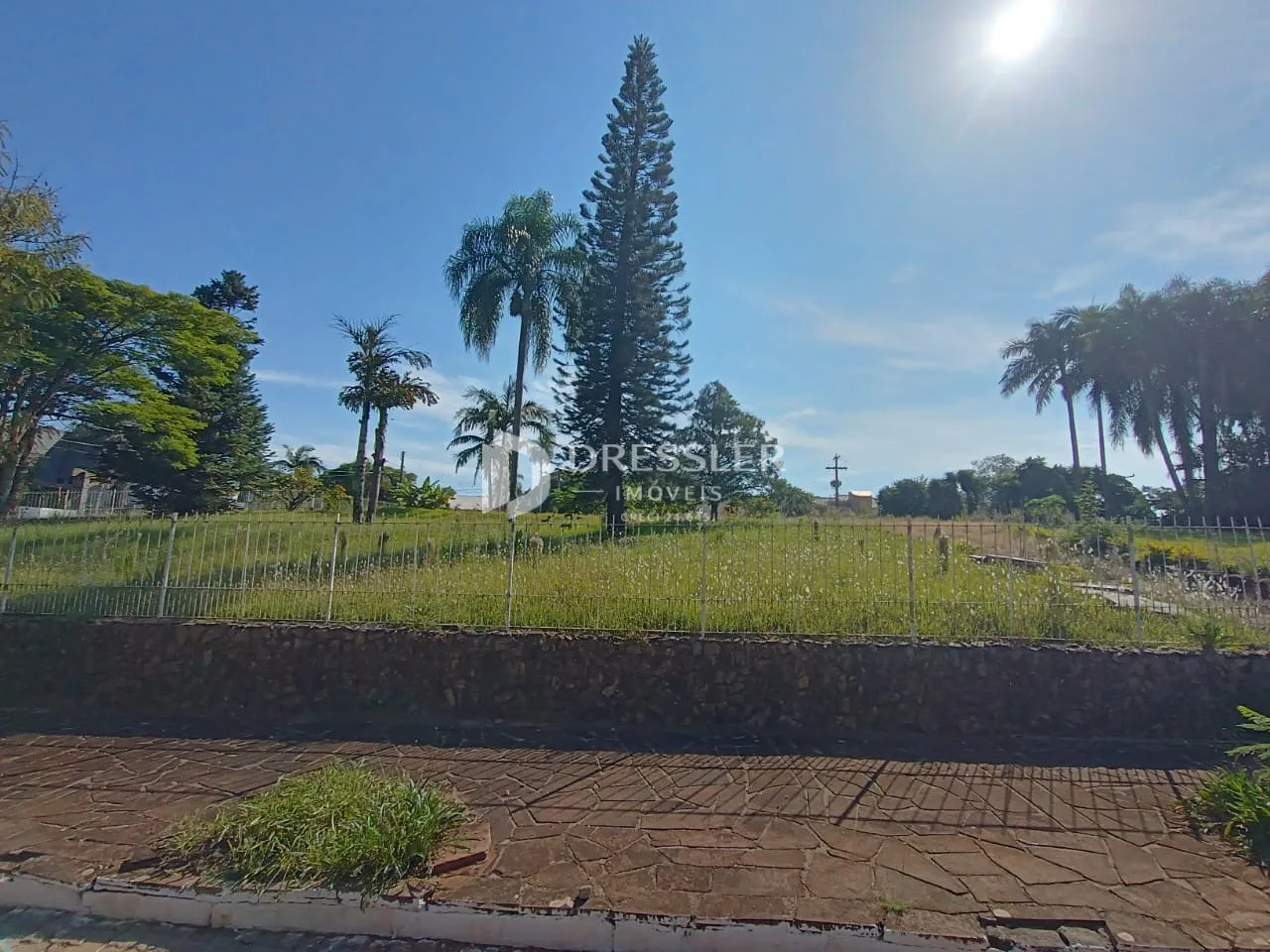 Vista externa da propriedade com campo gramado e muro de pedra.