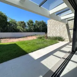 Vista de uma área externa com piso claro e vegetação ao fundo.