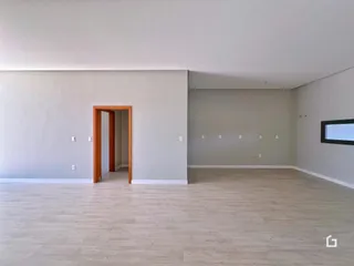 Uma sala de estar ampla com piso de madeira clara e paredes brancas.