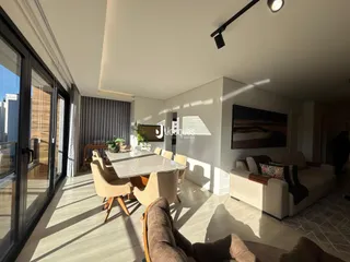 Sala de jantar iluminada com mesa de vidro e sofá no interior de uma residência.