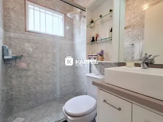 Banheiro com revestimento de mármore e box de vidro transparente.