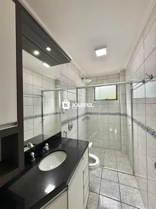 Um banheiro com revestimento de azulejos e box de vidro é mostrado na imagem.