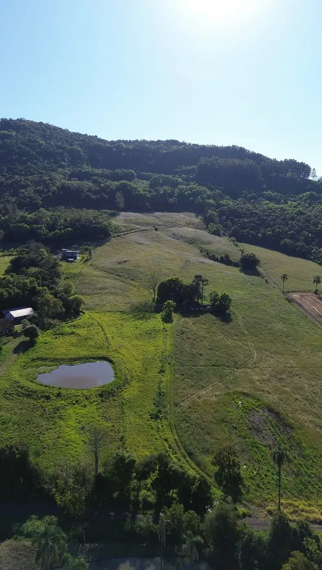 Vista aérea de uma paisagem rural com colinas verdes e um pequeno lago.
