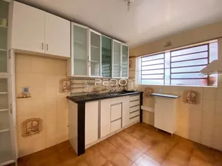 Vista interna de uma cozinha com armários brancos e piso de cerâmica.