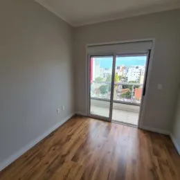 Foto do interior de um cômodo com piso de madeira e porta de vidro que dá para a vista externa.