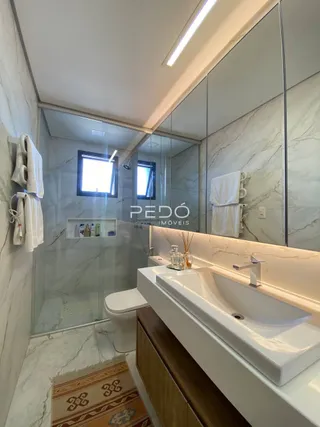 Banheiro com revestimento em mármore e box de vidro.