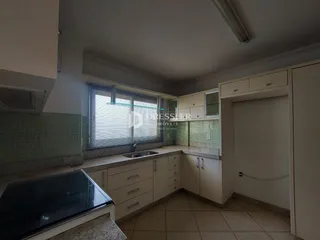 Interior de uma cozinha com armários brancos e revestimento de azulejos claros.