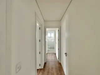 Corredor interno de uma residência com paredes brancas e piso de madeira.
