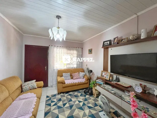 Sala de estar com sofá bege e televisão montada na parede.