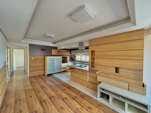 Sala de estar e cozinha com piso de madeira clara e armários de madeira.