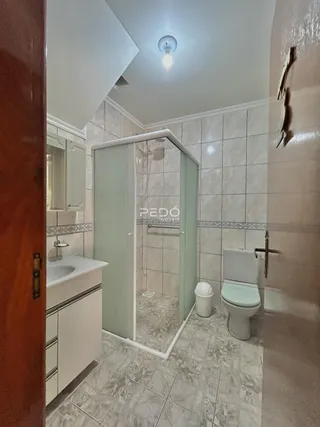 Foto interna de um banheiro com box de vidro e revestimento cerâmico.