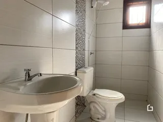 Banheiro com louças sanitárias brancas e revestimento de azulejos brancos.