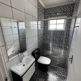 Banheiro com revestimento de azulejos escuros e bancada branca.