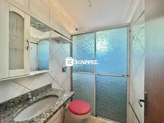 Banheiro com bancada de mármore e box de vidro transparente.