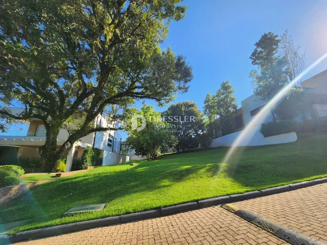 Vista externa de uma propriedade com gramado verde e árvores sob um céu azul.