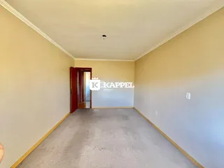 Um corredor longo com paredes bege e piso de carpete cinza.