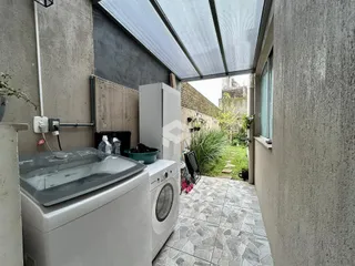 Vista externa de um pátio com paredes de concreto e um jardim ao fundo.